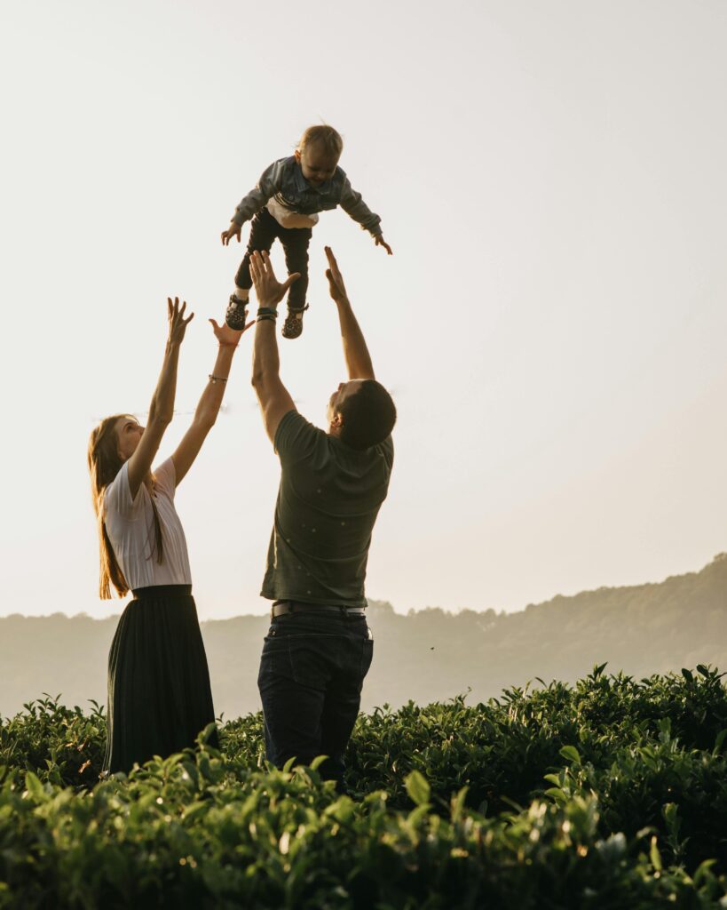 Side view of parents in casual clothes throwing excited son up while standing among lush green bushes in summer