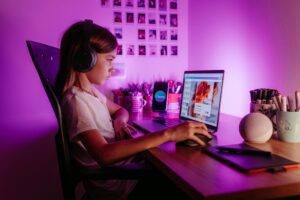 Child focused on laptop wearing headphones at desk with purple lighting. Modern tech scene.